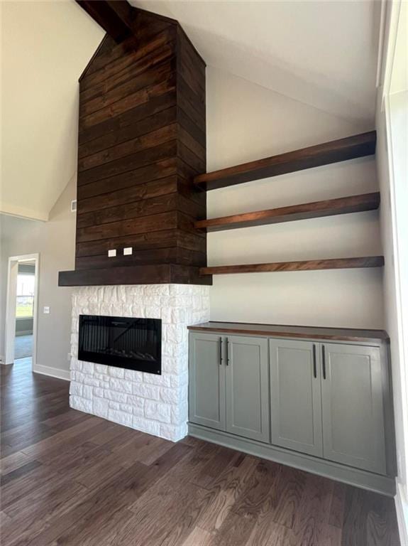 unfurnished living room with vaulted ceiling with beams, dark wood-style flooring, a fireplace, and baseboards