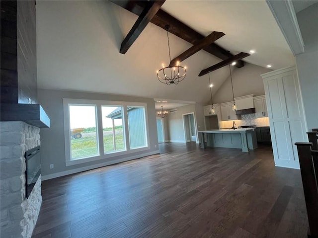 unfurnished living room with dark wood-style floors, a fireplace, beam ceiling, and an inviting chandelier