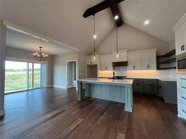 kitchen featuring decorative light fixtures, tasteful backsplash, light countertops, a kitchen island with sink, and beamed ceiling