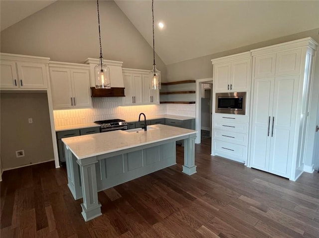 kitchen with hanging light fixtures, a kitchen island with sink, stainless steel appliances, white cabinetry, and open shelves