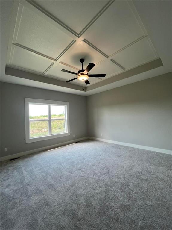 carpeted spare room with coffered ceiling, baseboards, a raised ceiling, and a ceiling fan