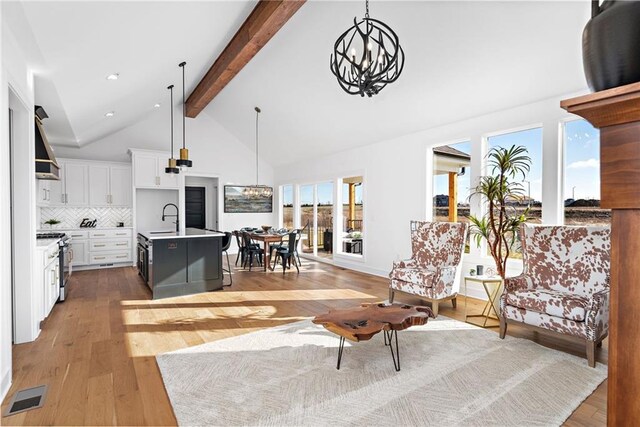 living room with high vaulted ceiling, sink, a notable chandelier, light hardwood / wood-style floors, and beam ceiling