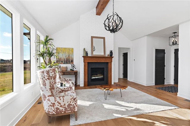 sitting room featuring a notable chandelier, light hardwood / wood-style floors, a large fireplace, and vaulted ceiling with beams