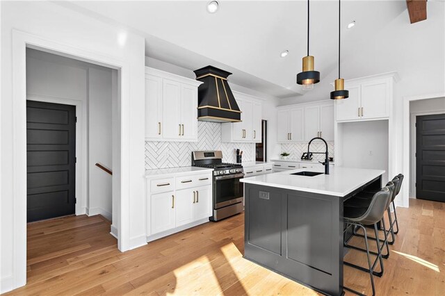 kitchen featuring sink, white cabinets, custom exhaust hood, a kitchen island with sink, and stainless steel gas range