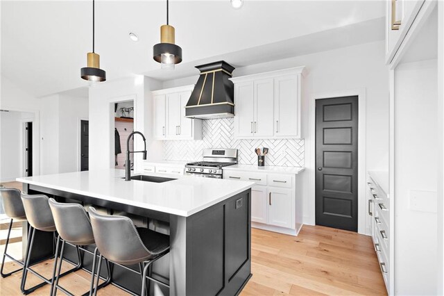 kitchen featuring sink, a center island with sink, stainless steel range with gas cooktop, pendant lighting, and white cabinets