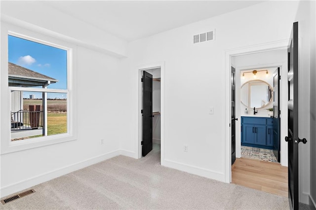 unfurnished bedroom featuring baseboards, a spacious closet, visible vents, and light colored carpet