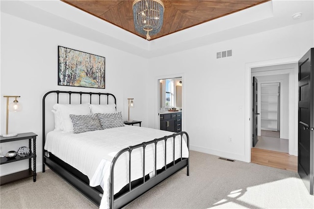 bedroom with ensuite bath, a tray ceiling, light carpet, wooden ceiling, and a chandelier