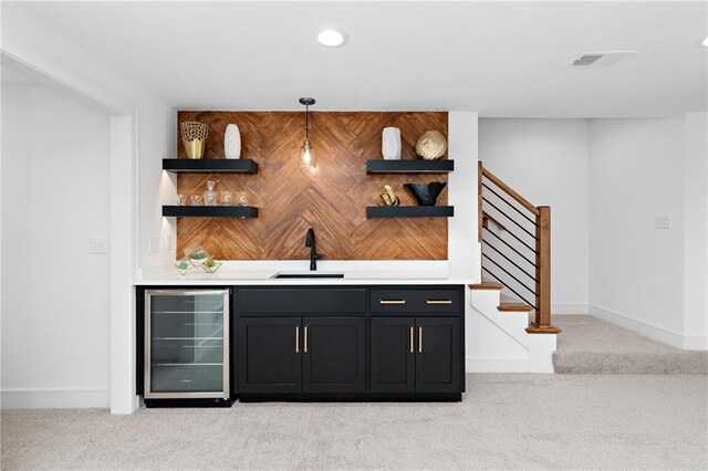 bar featuring light colored carpet, beverage cooler, sink, and hanging light fixtures