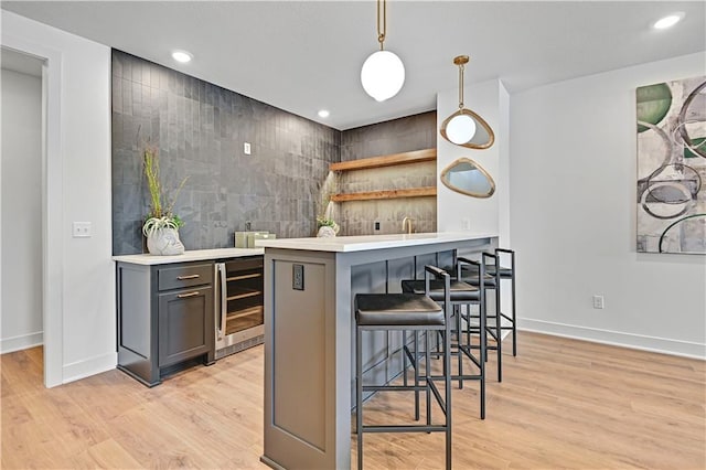 bar featuring gray cabinets, light hardwood / wood-style floors, hanging light fixtures, and beverage cooler