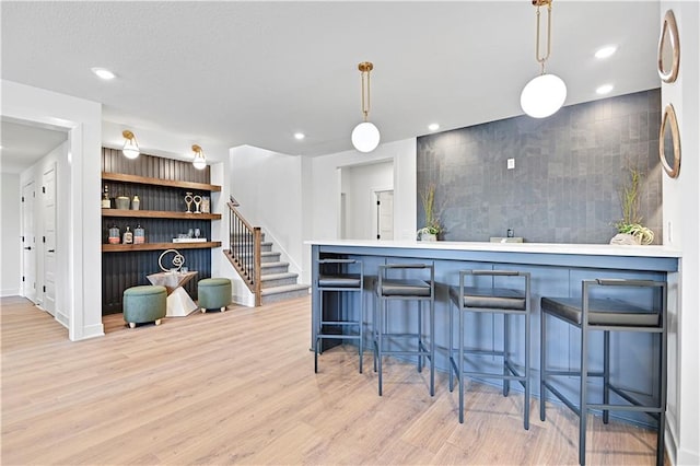 kitchen with a kitchen bar, pendant lighting, light hardwood / wood-style flooring, and tile walls