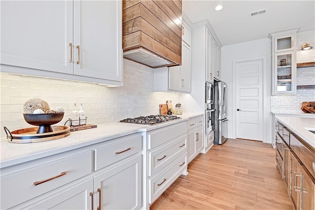 17433 Gillette St, Overland Park, KS 66221 - kitchen with wall chimney range hood, appliances with stainless steel finishes, white cabinetry, backsplash, and glass insert cabinets
