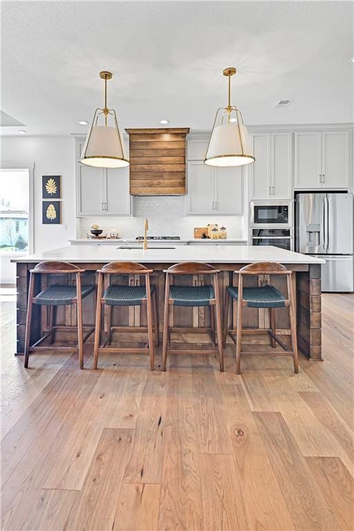 17433 Gillette St, Overland Park, KS 66221 - kitchen with appliances with stainless steel finishes, light wood-style floors, light countertops, a large island with sink, and a kitchen bar