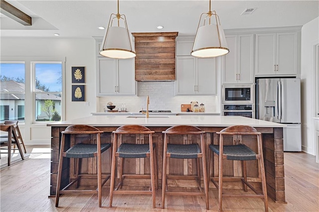 17433 Gillette St, Overland Park, KS 66221 - kitchen featuring stainless steel appliances, a kitchen island with sink, decorative backsplash, light wood-style floors, and light countertops