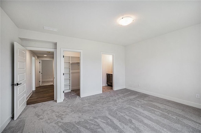 unfurnished bedroom featuring a walk in closet, light carpet, connected bathroom, and a closet