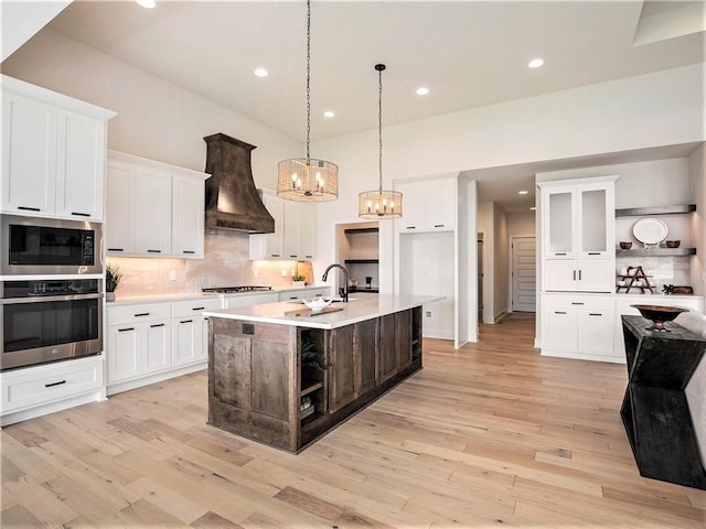 kitchen with white cabinetry, custom exhaust hood, stainless steel appliances, and a center island with sink