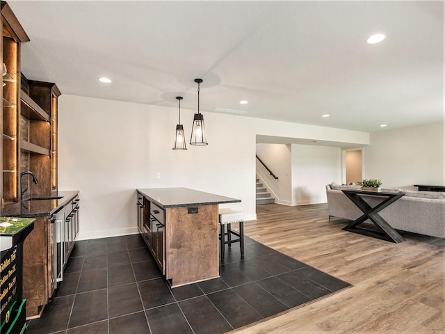 kitchen with sink, dark wood-type flooring, a kitchen bar, decorative light fixtures, and dark stone counters