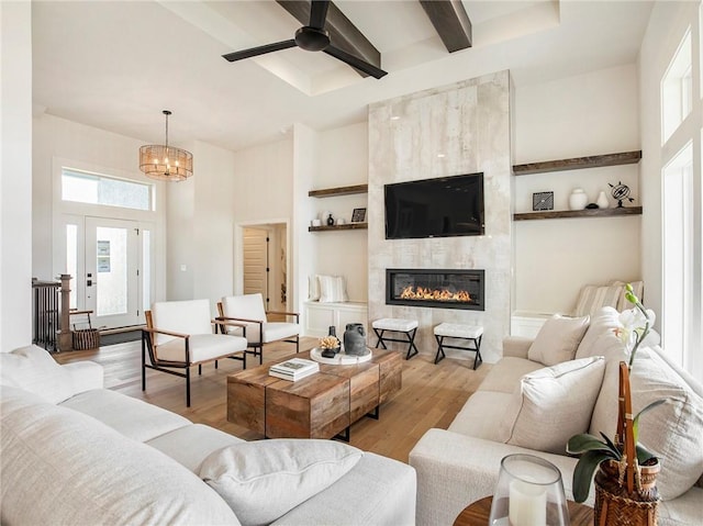 living room featuring a tiled fireplace, ceiling fan with notable chandelier, beam ceiling, and wood finished floors
