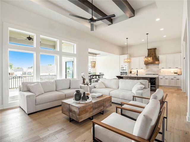 living room with a towering ceiling, recessed lighting, light wood-style flooring, a ceiling fan, and beamed ceiling