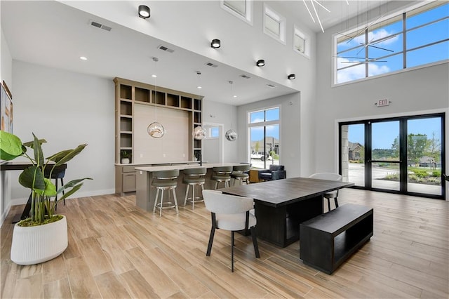 dining area featuring a towering ceiling, a notable chandelier, and light wood-type flooring