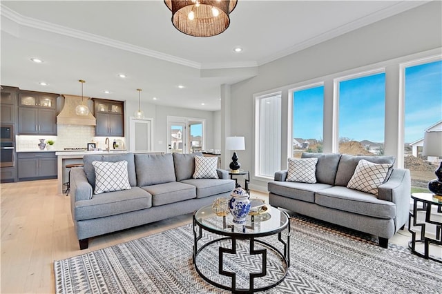 living room with sink, light wood-type flooring, crown molding, and a wealth of natural light