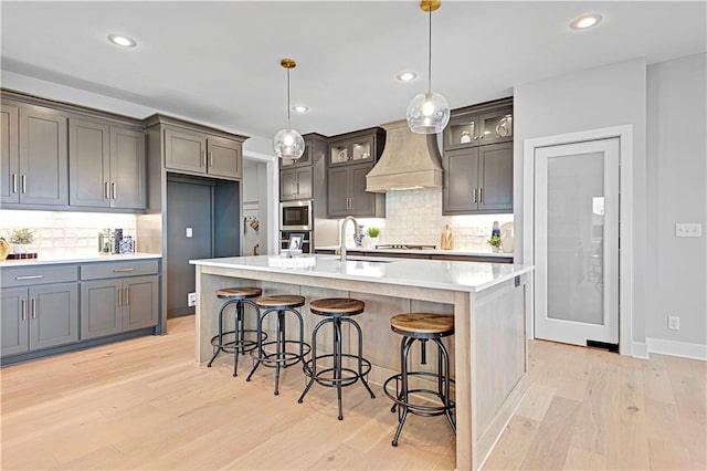 kitchen with light hardwood / wood-style floors, sink, custom range hood, and an island with sink