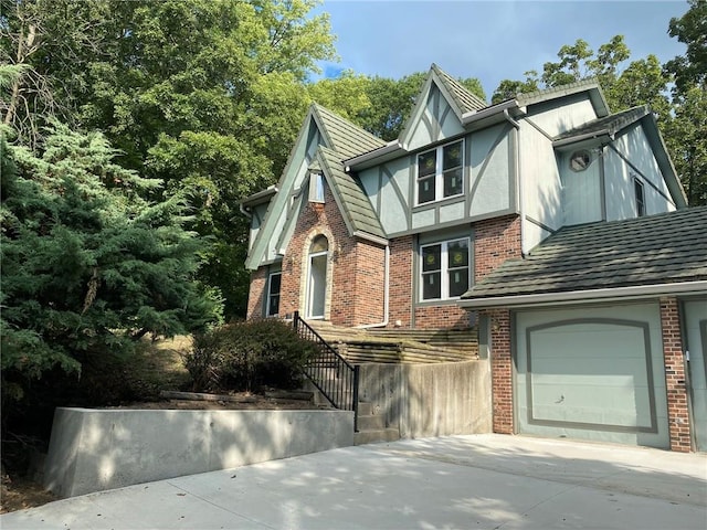 english style home with a garage, concrete driveway, brick siding, and stucco siding