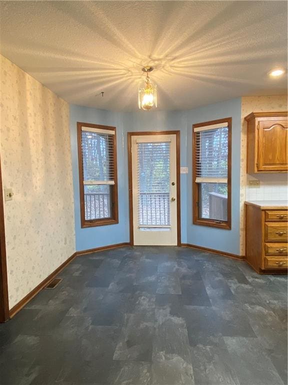 doorway to outside featuring baseboards, a textured ceiling, and wallpapered walls