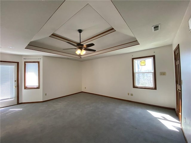 unfurnished room with a tray ceiling, visible vents, carpet flooring, ceiling fan, and baseboards