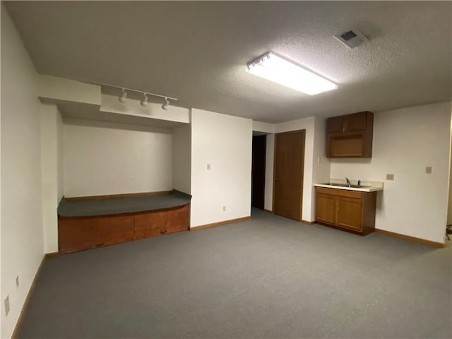 finished basement with rail lighting, carpet flooring, a sink, a textured ceiling, and baseboards