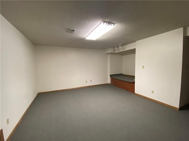 finished below grade area with a textured ceiling, carpet floors, visible vents, and baseboards