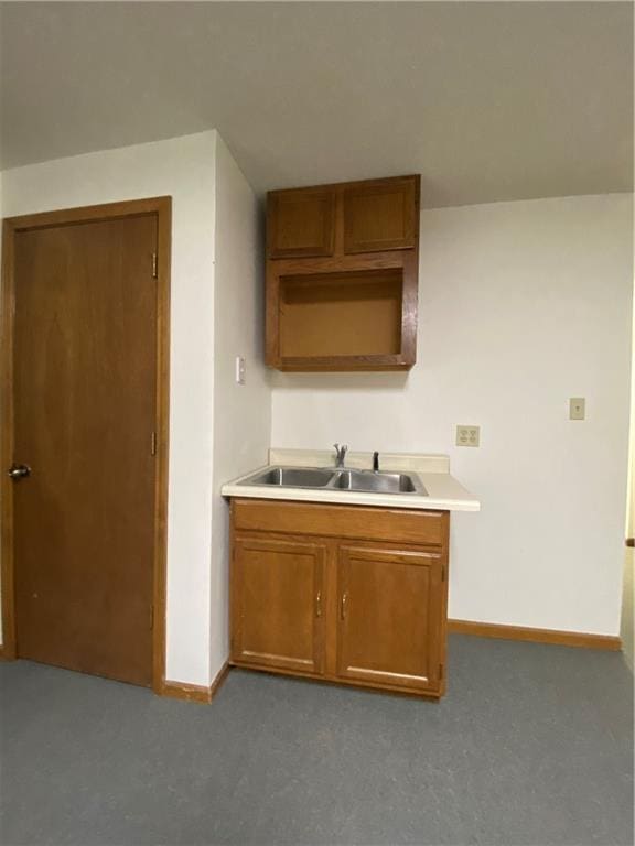 kitchen with brown cabinetry, light countertops, a sink, and baseboards