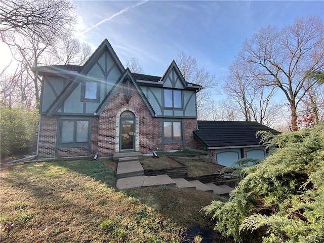 tudor home featuring a garage, a front yard, brick siding, and stucco siding