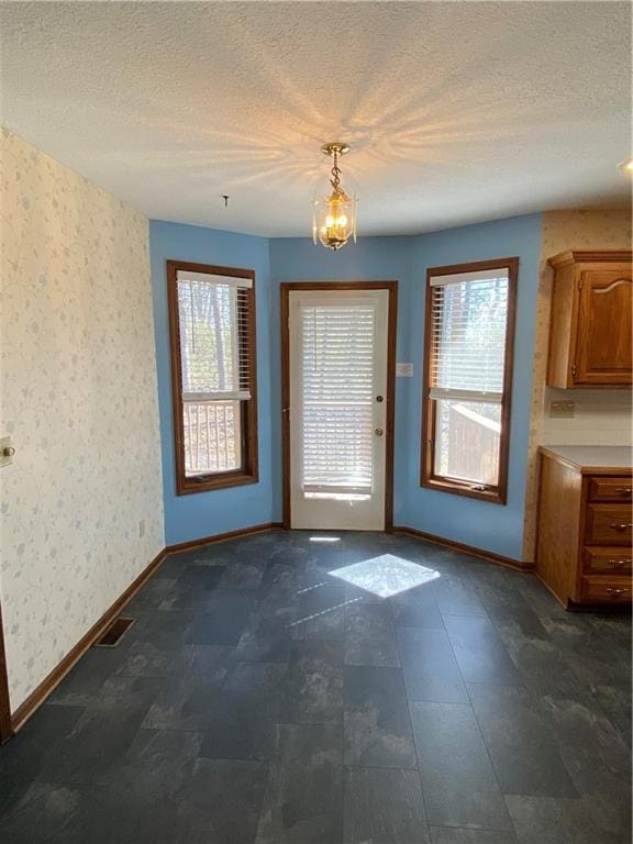 doorway with a textured ceiling, a wealth of natural light, and wallpapered walls