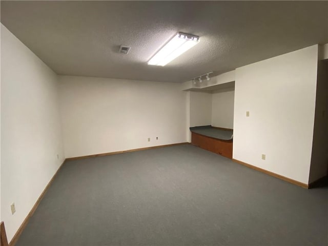 finished below grade area featuring a textured ceiling, carpet floors, visible vents, and baseboards