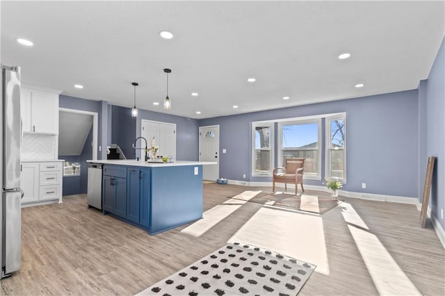 kitchen with tasteful backsplash, a center island with sink, white cabinets, hanging light fixtures, and light wood-type flooring