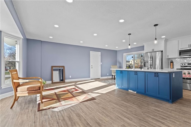 kitchen with pendant lighting, light wood-type flooring, an island with sink, stainless steel appliances, and white cabinetry