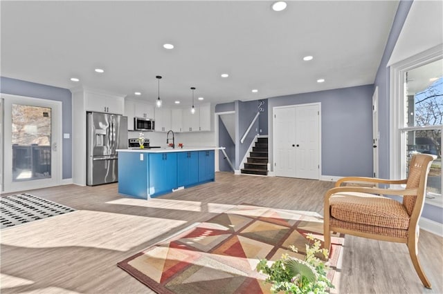 kitchen with decorative light fixtures, white cabinets, an island with sink, stainless steel appliances, and light wood-type flooring