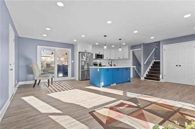 kitchen featuring decorative light fixtures, white cabinetry, an island with sink, stainless steel appliances, and light wood-type flooring