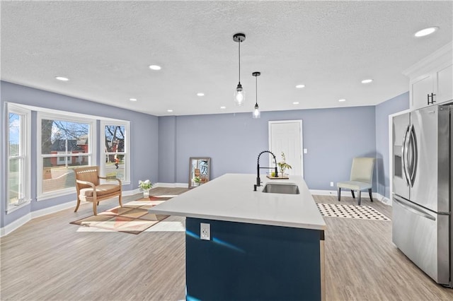 kitchen with an island with sink, sink, hanging light fixtures, stainless steel refrigerator with ice dispenser, and light wood-type flooring