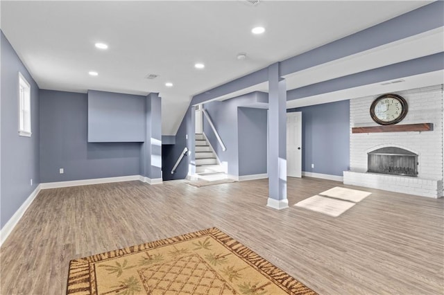 basement with a brick fireplace, light hardwood / wood-style flooring, and brick wall