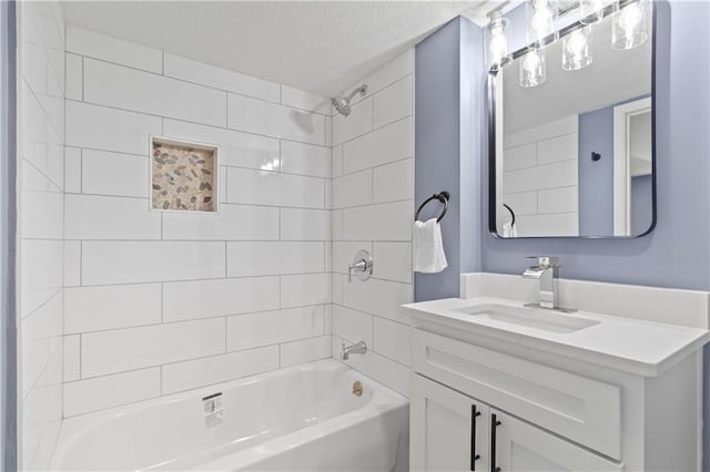 bathroom with a textured ceiling, tiled shower / bath, and vanity