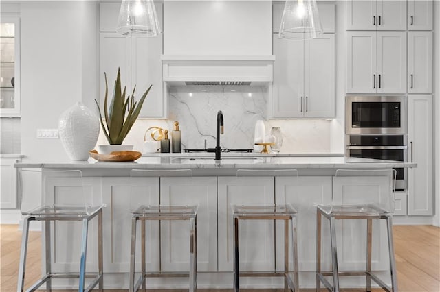 kitchen with built in microwave, a center island with sink, oven, decorative backsplash, and white cabinets