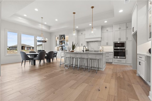 kitchen featuring a kitchen island with sink, a tray ceiling, oven, and white cabinets