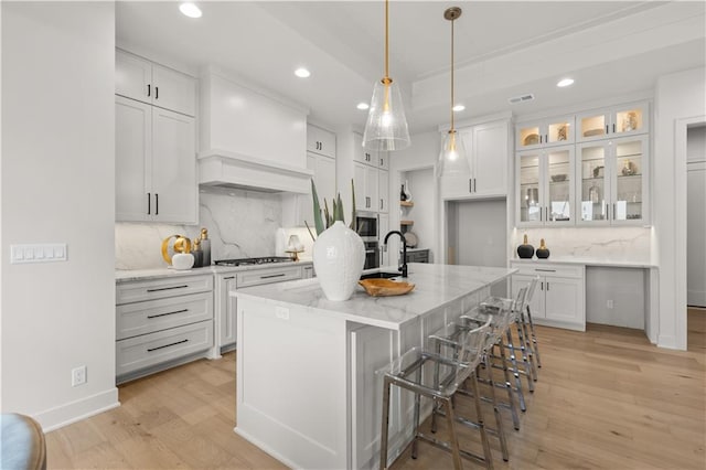 kitchen with light stone countertops, white cabinets, a center island with sink, decorative backsplash, and decorative light fixtures