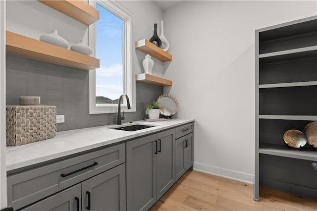 kitchen featuring sink, gray cabinetry, backsplash, light stone counters, and light wood-type flooring