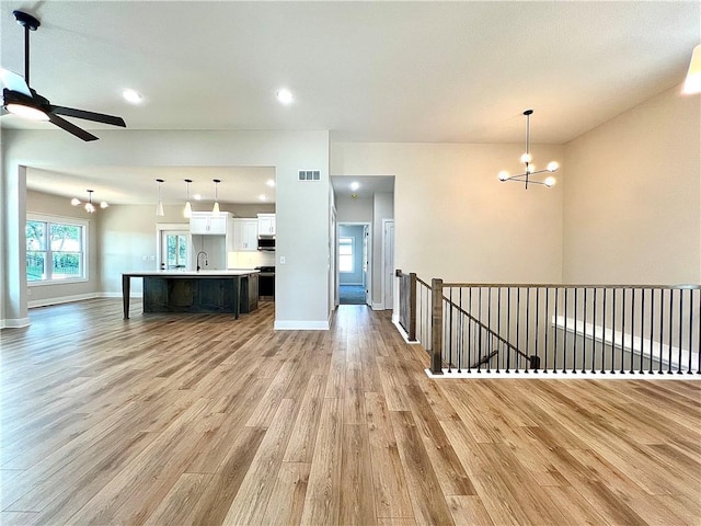 unfurnished living room featuring ceiling fan with notable chandelier and light wood-type flooring