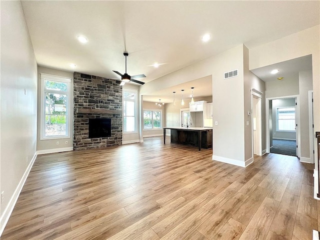 unfurnished living room featuring ceiling fan, sink, light hardwood / wood-style flooring, and a fireplace