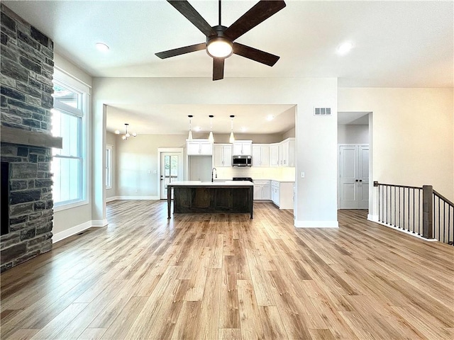 kitchen with light wood-type flooring, decorative light fixtures, white cabinets, and a kitchen island with sink