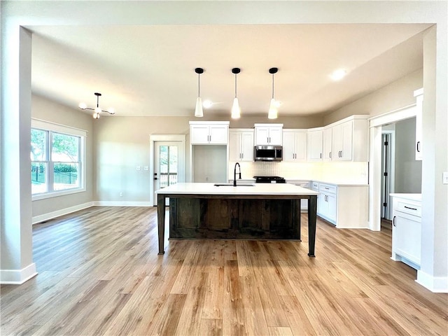 kitchen with decorative light fixtures, light hardwood / wood-style floors, white cabinetry, and a center island with sink