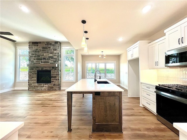 kitchen with white cabinets, decorative light fixtures, an island with sink, sink, and gas range oven